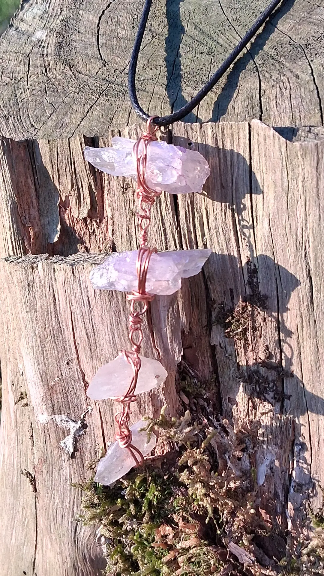 A wand of rose quartz, hand-wrapped in copper, resting on a weathered stump