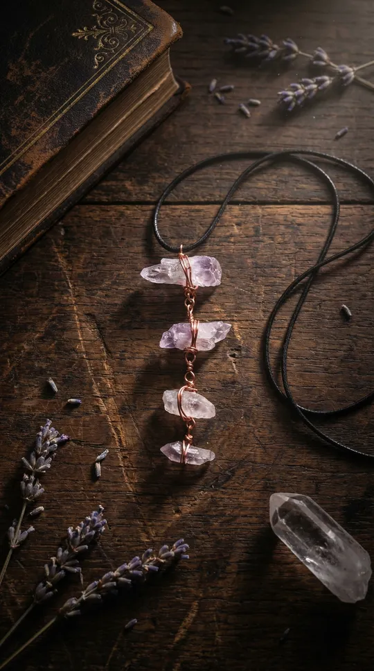 A wire-wrapped amethyst and quartz pendant necklace resting on a weathered wooden table beside lavender and an old book
