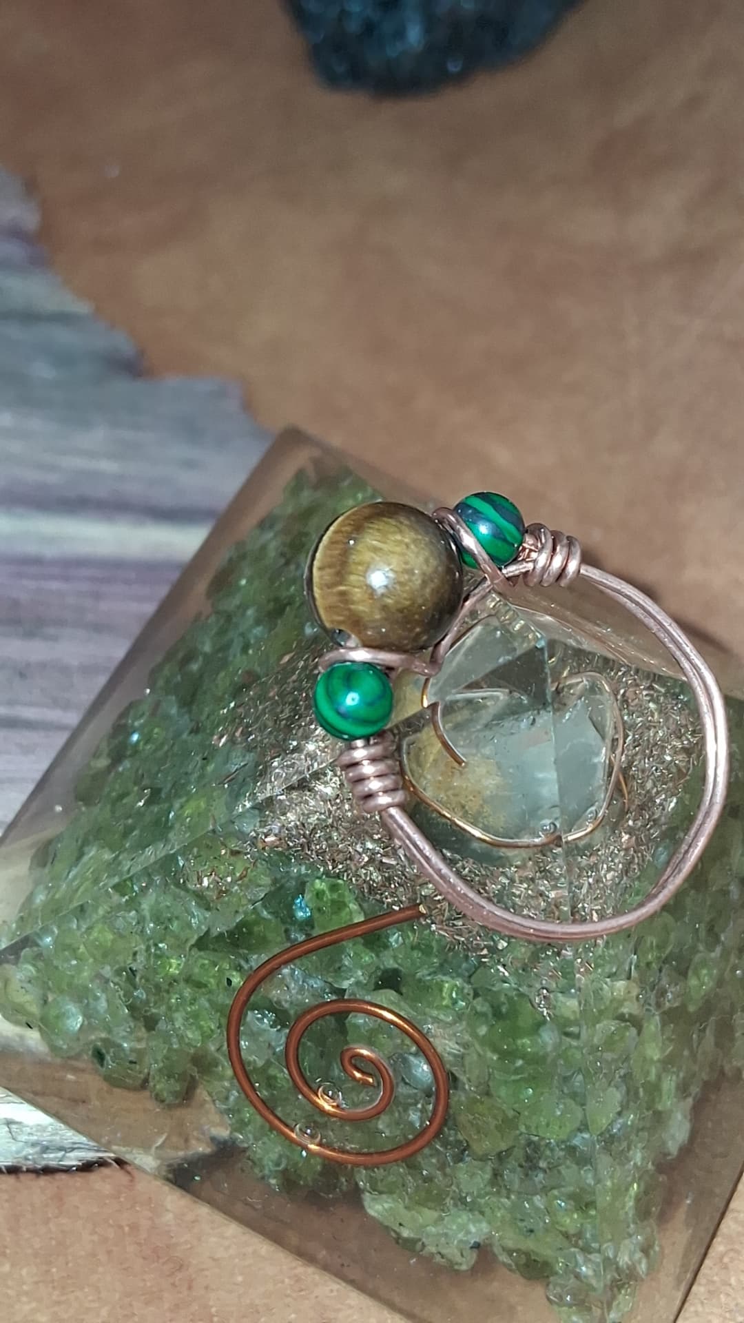 A copper wire-wrapped ring with tiger's eye and malachite beads, close-up on a green crystal