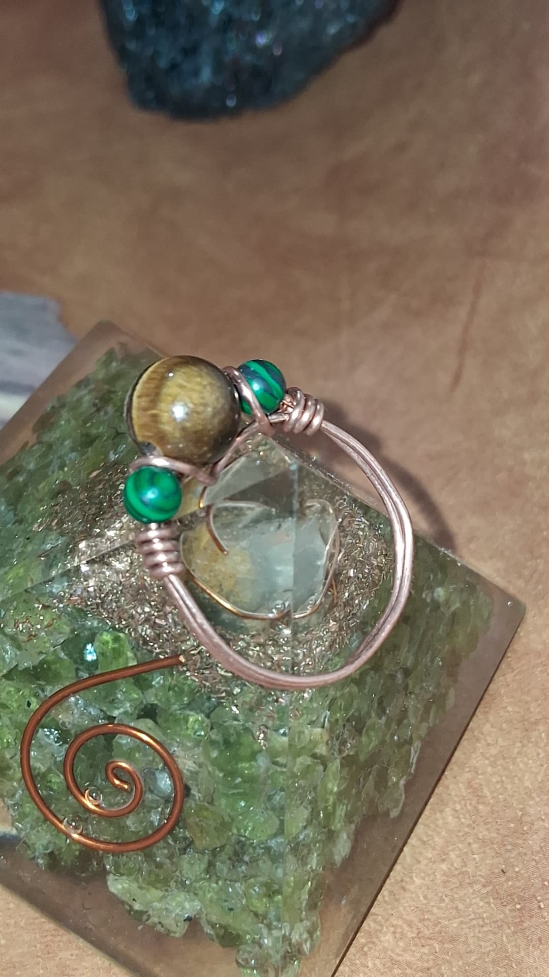 A copper wire-wrapped ring with tiger's eye and green malachite beads on a green crystal pyramid